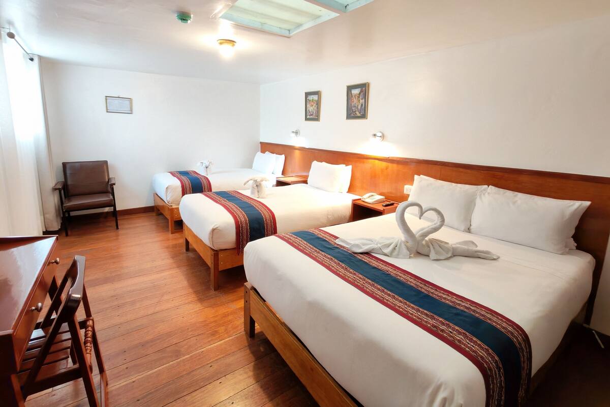 A hotel room with two beds, a wooden chair, a desk, and a skylight.
