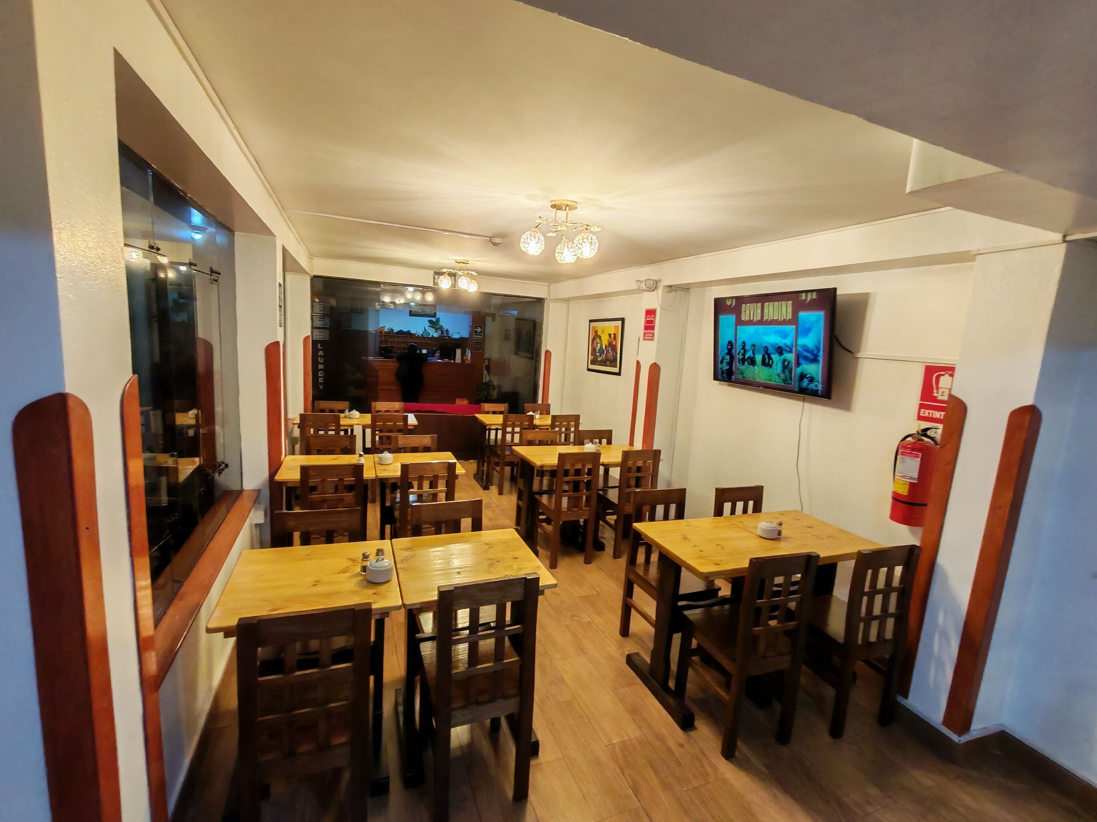 A restaurant interior with wooden tables and chairs, a counter, a fire extinguisher, and a wall-mounted television.