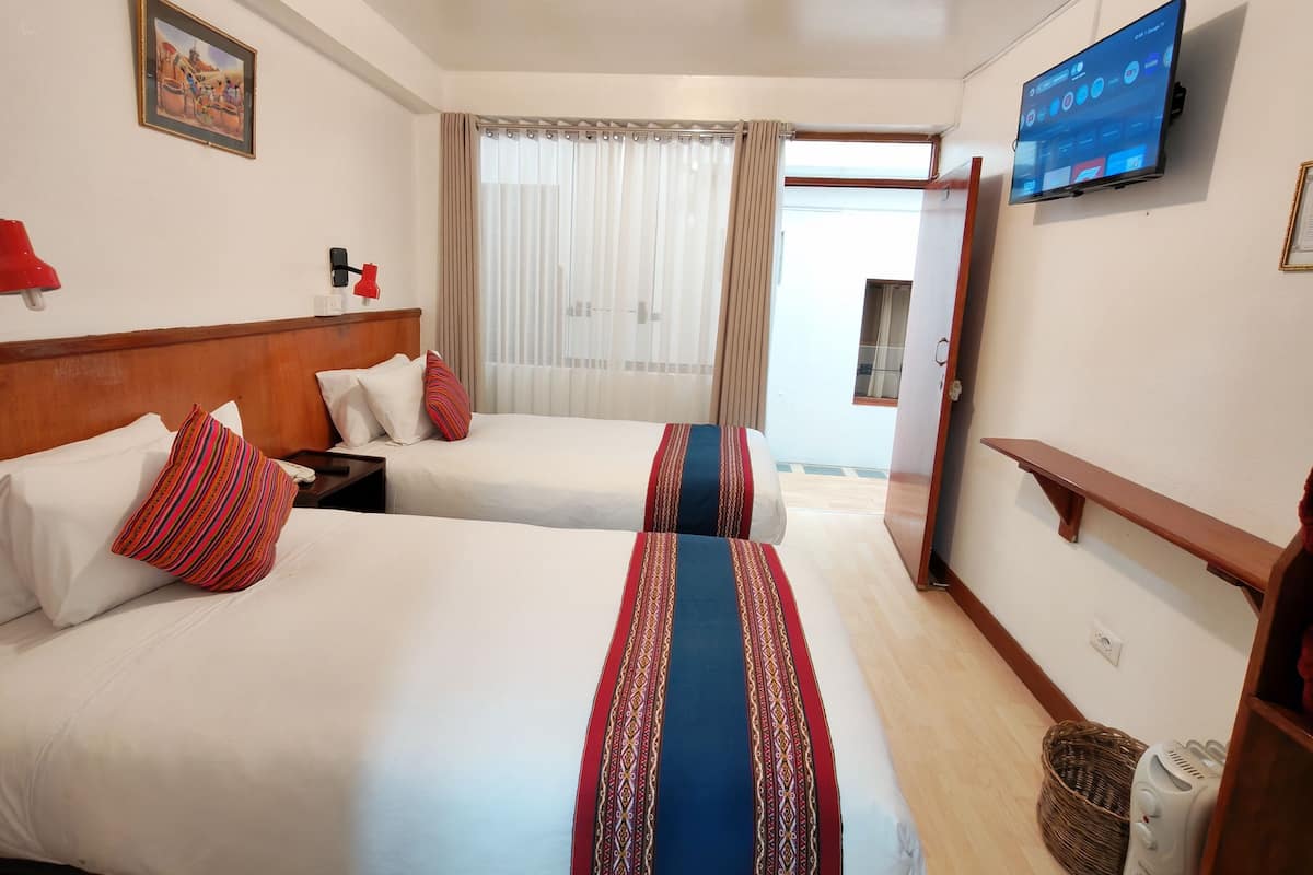 A hotel room with two beds, a TV, a window with curtains, and a wooden bench.