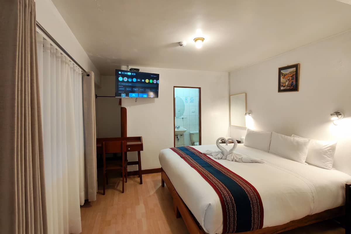 A hotel room with a bed, a television mounted on the wall, a desk, and a chair.