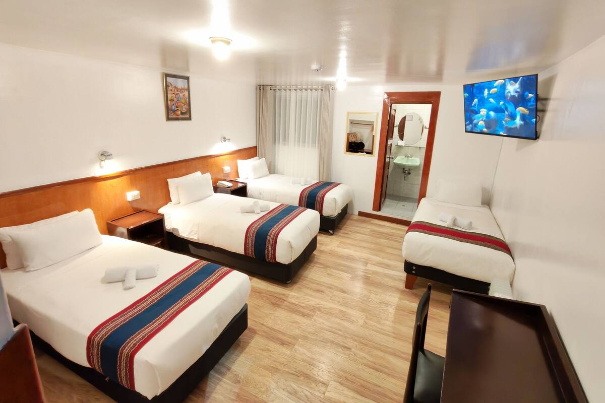 A hotel room with two beds, a sofa, a TV, a bathroom with a mirror, and a painting on the wall.