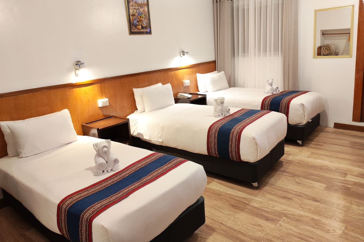 A hotel room with three beds, a wooden headboard, a painting on the wall, and a window with curtains.
