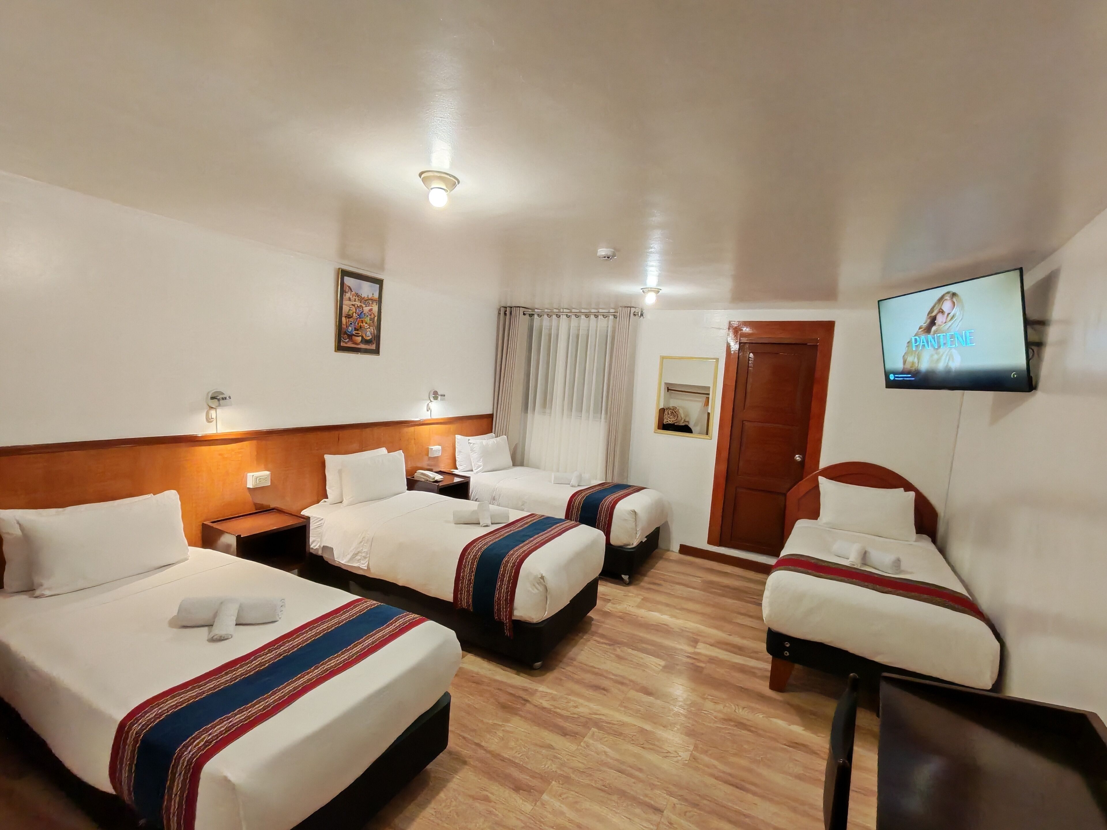 A hotel room with three beds, a television, a wooden headboard, a nightstand with a phone, and a painting on the wall.