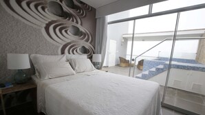Una habitación de hotel moderna con una cama grande, una mesita de noche, una lámpara y vistas a una zona de piscina a través de una puerta de cristal.