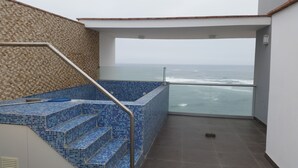 Un balcón con vistas al océano, una zona de piscina con azulejos y una escalera con barandilla de metal.