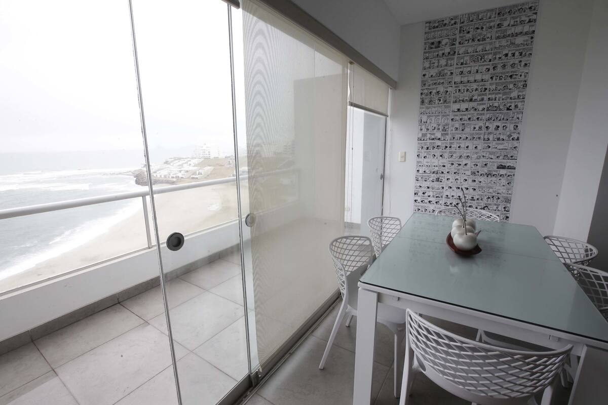A balcony with a glass door, a white table with chairs, and a wall with black and white photos.