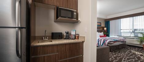 Una cocina compacta con un refrigerador de acero inoxidable, un microondas y una cafetera.