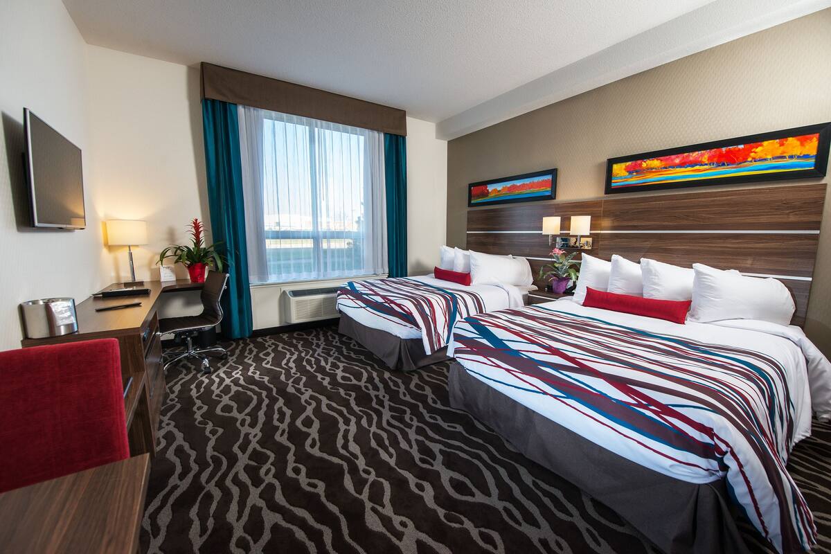 A hotel room with two beds, a desk, a chair, a TV, and a window with curtains.