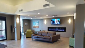A modern lobby with a brown leather sofa, a television mounted on the wall, and a reception desk. - Encore Suites by Service Plus Inns (Grande Prairie)