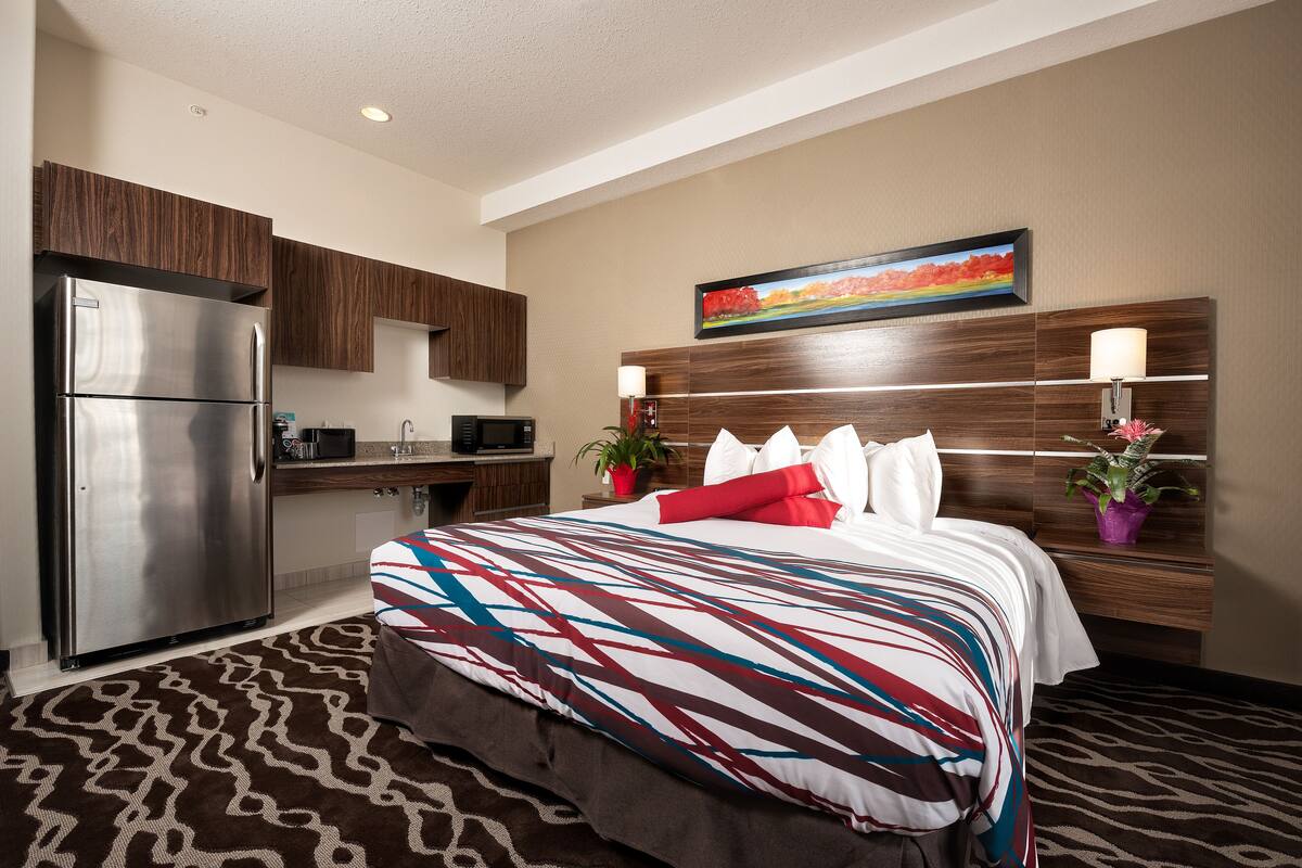 A hotel room with a bed, a refrigerator, a microwave, and a wooden cabinet.