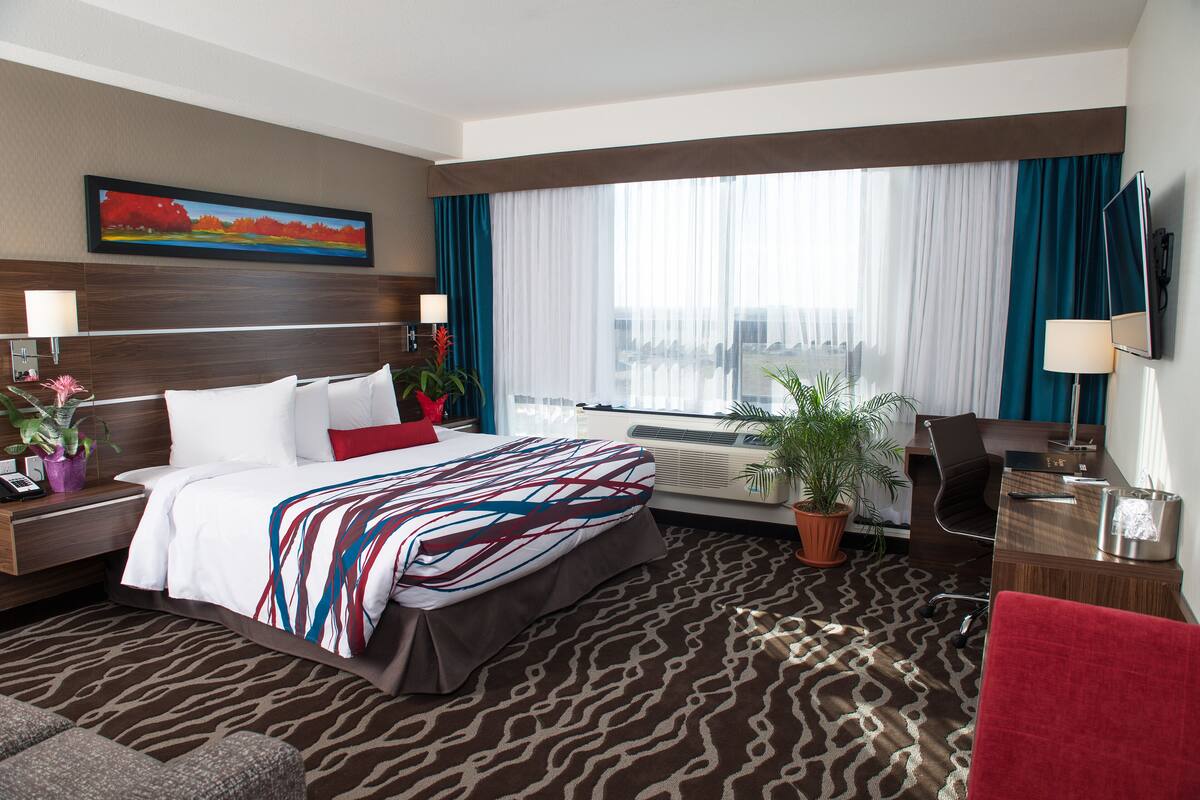 A hotel room with a large bed, a desk, a chair, a TV, and a window with curtains.