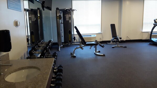 A gym with various exercise equipment including dumbbells, a bench press, and a treadmill.