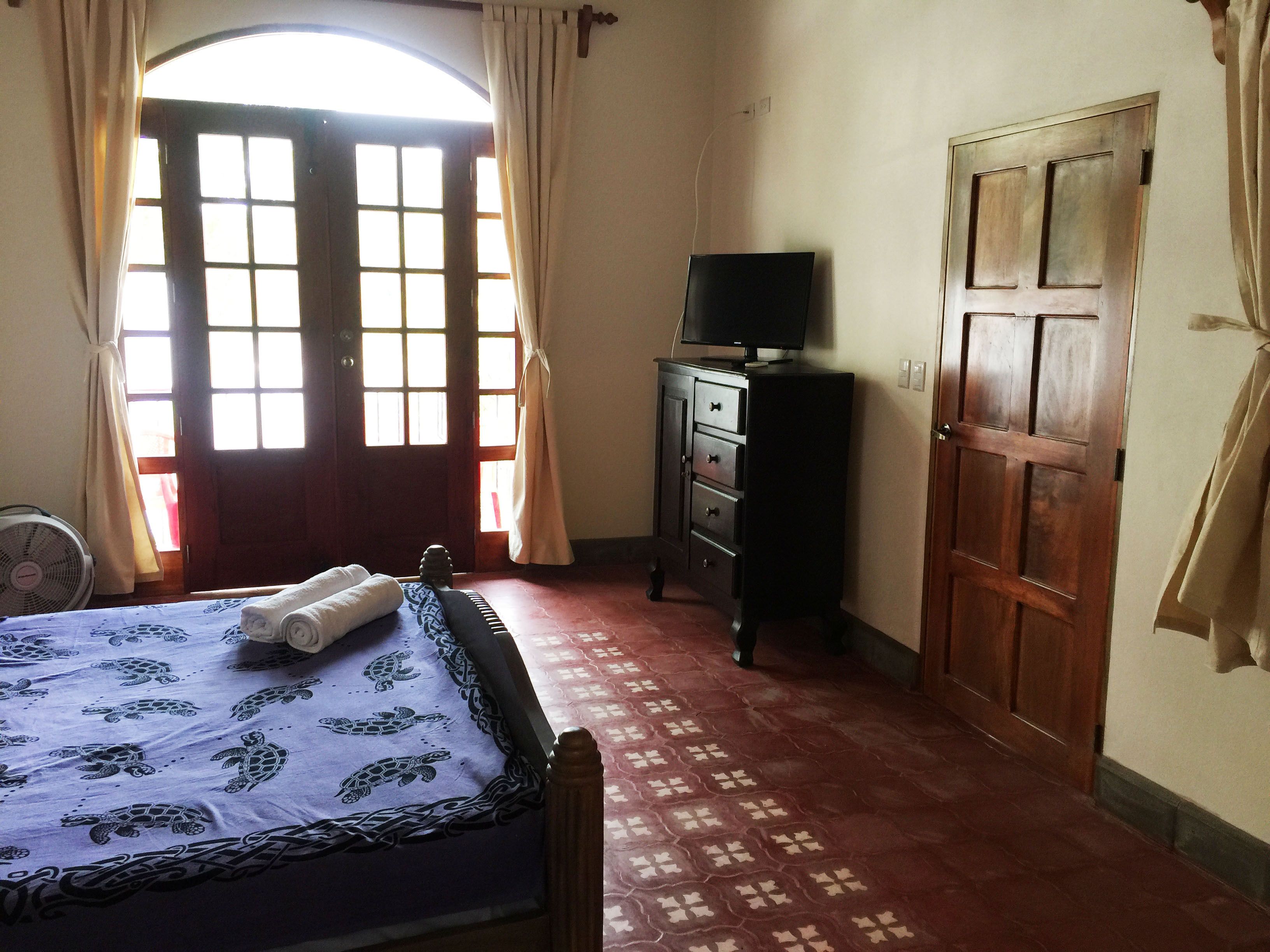 A bedroom with a bed, a dresser, a television, and a door.
