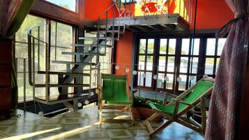 Relax in this spacious room with a high ceiling, featuring a vibrant wall, a wooden staircase, and large windows.