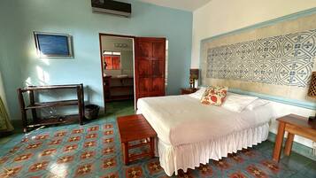Un dormitorio con una cama, una mesita de noche de madera, una pequeña mesa, un espejo y una puerta que da a un baño.