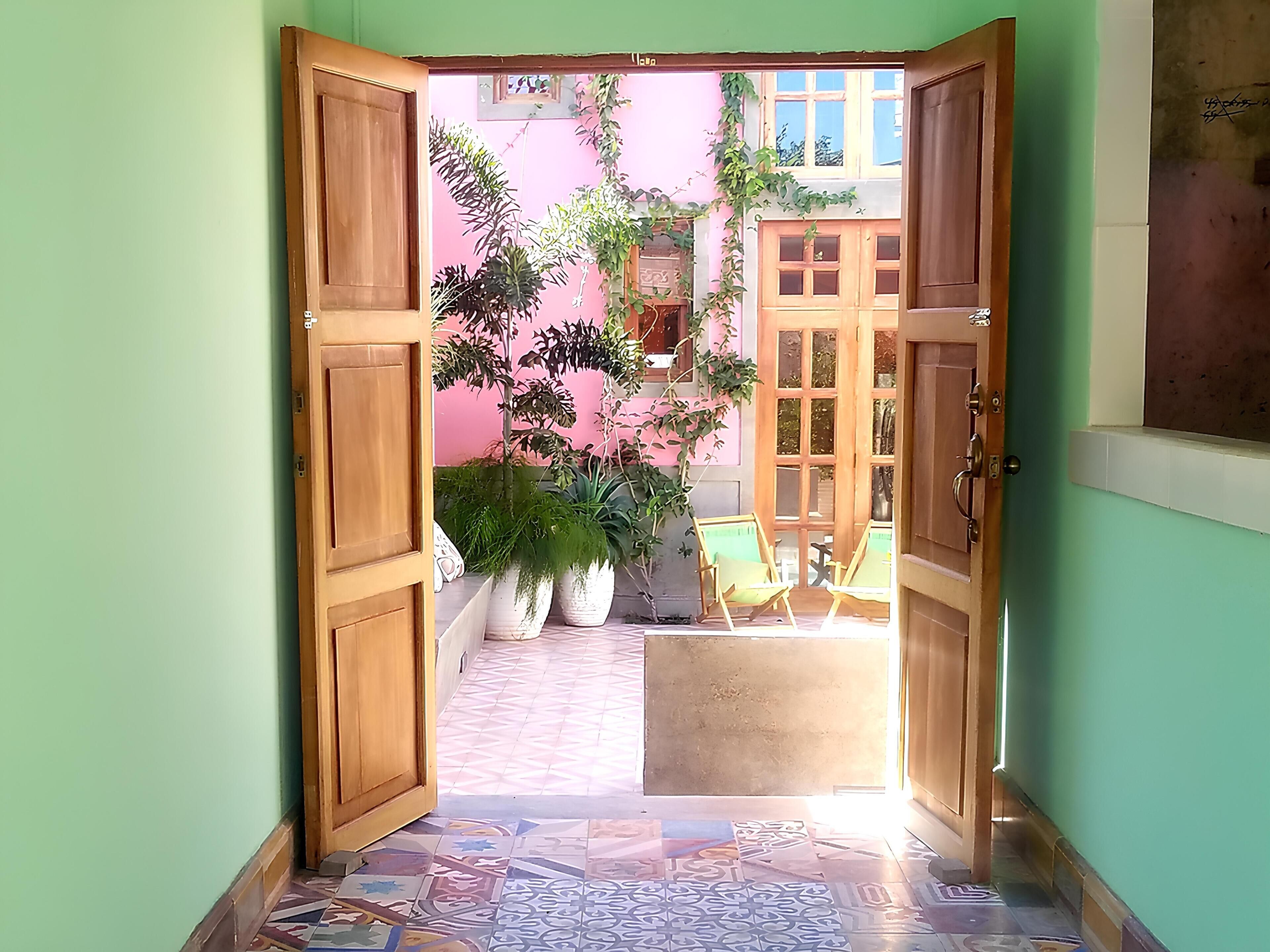 Una puerta abierta que da a un patio con baldosas, plantas en macetas y dos sillas.