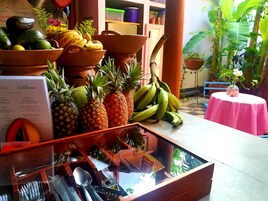 Una exhibición de frutas con aguacates, plátanos y piñas, un menú y una mesa con mantel rosa.