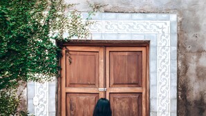 A woman in a pink dress walking towards a large wooden door with a decorative white border. - Hotel La Polvora (Granada)