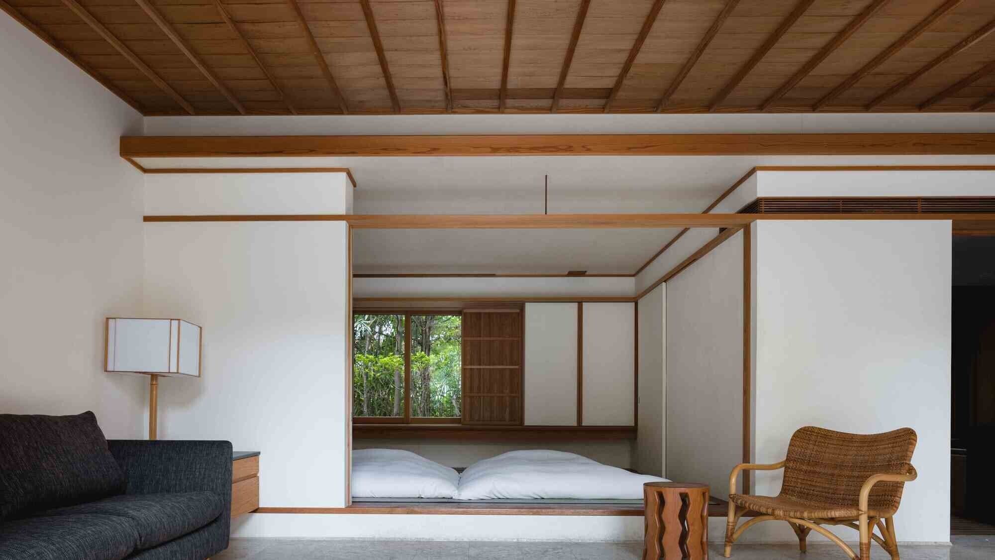 A minimalist room with a bed, a sofa, a chair, and a lamp.