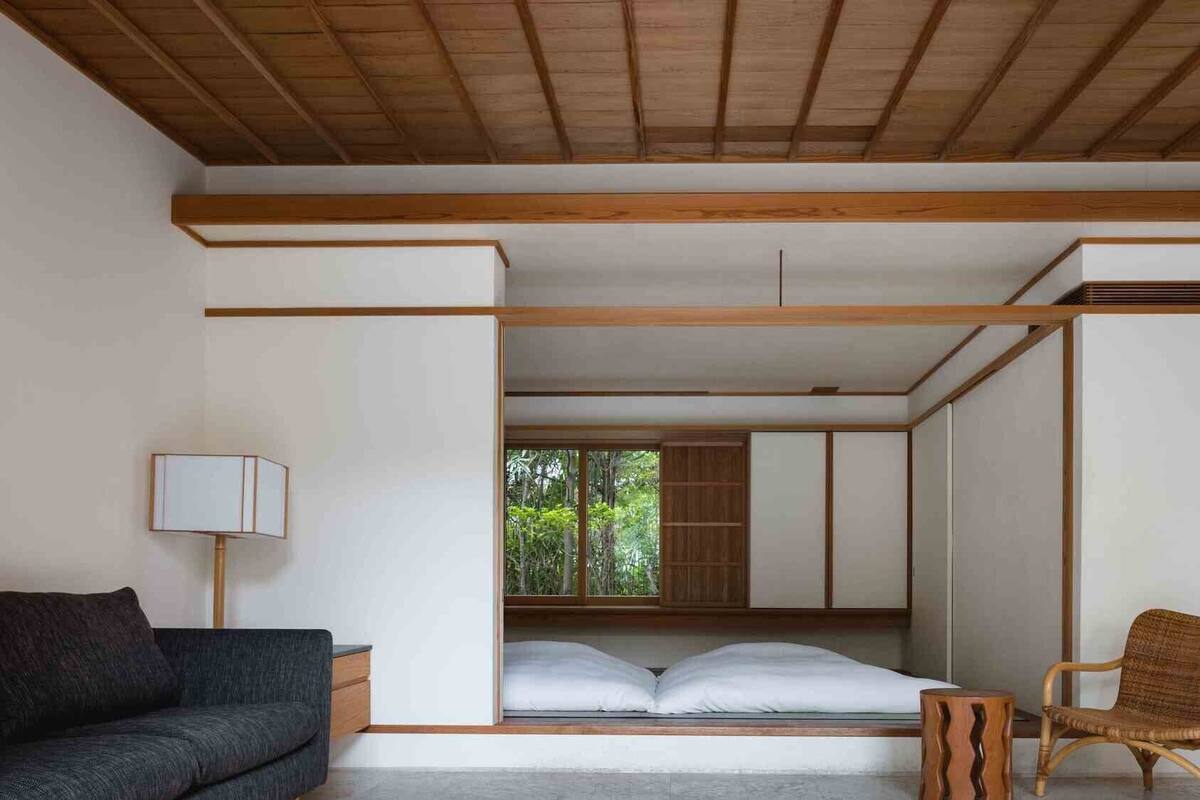 Ein schlicht eingerichteter Raum mit einem Bett, einer Couch, einem Sessel und einer Lampe.