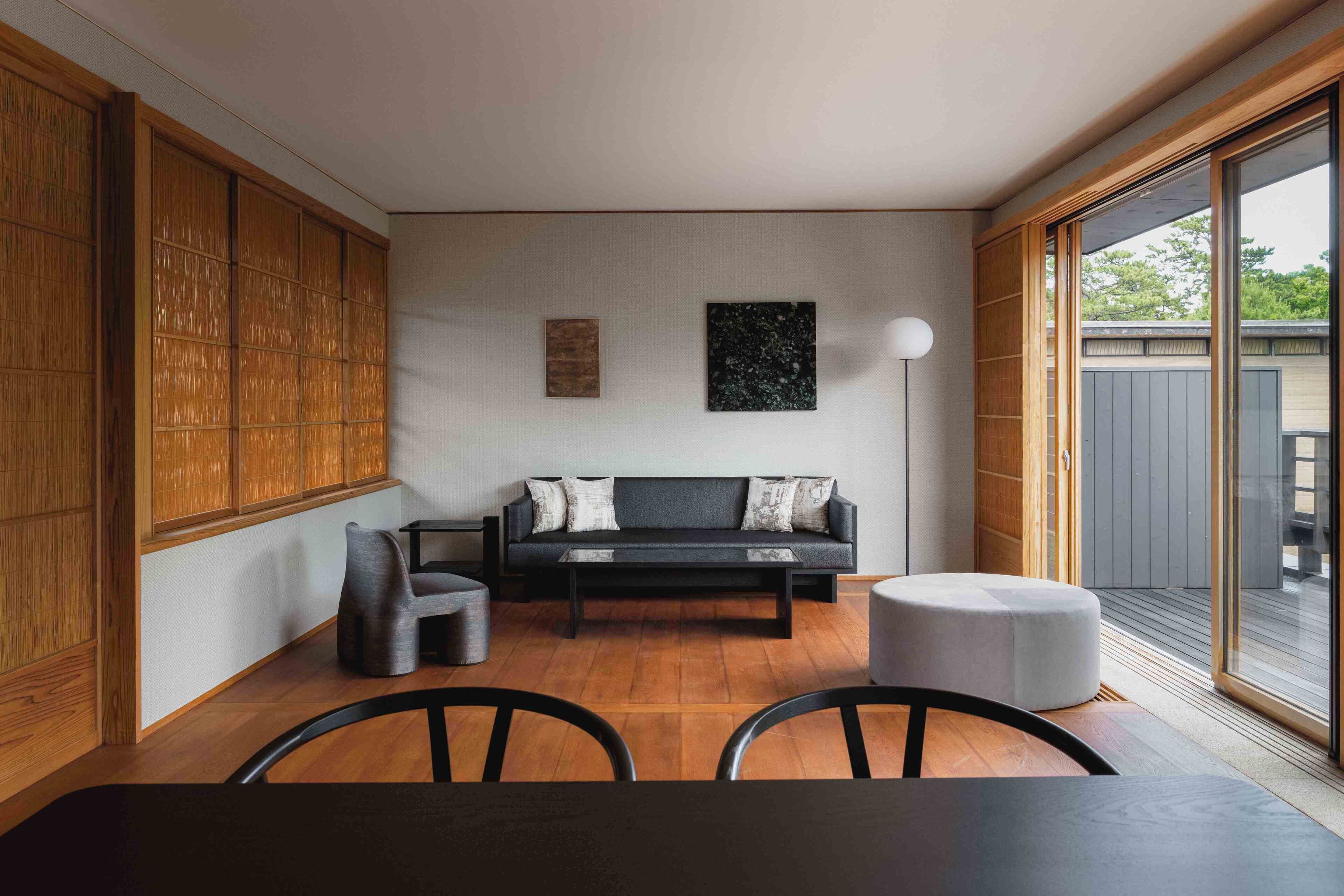 Un salon moderne avec un canapé noir, un pouf rond et une table à manger avec des chaises.