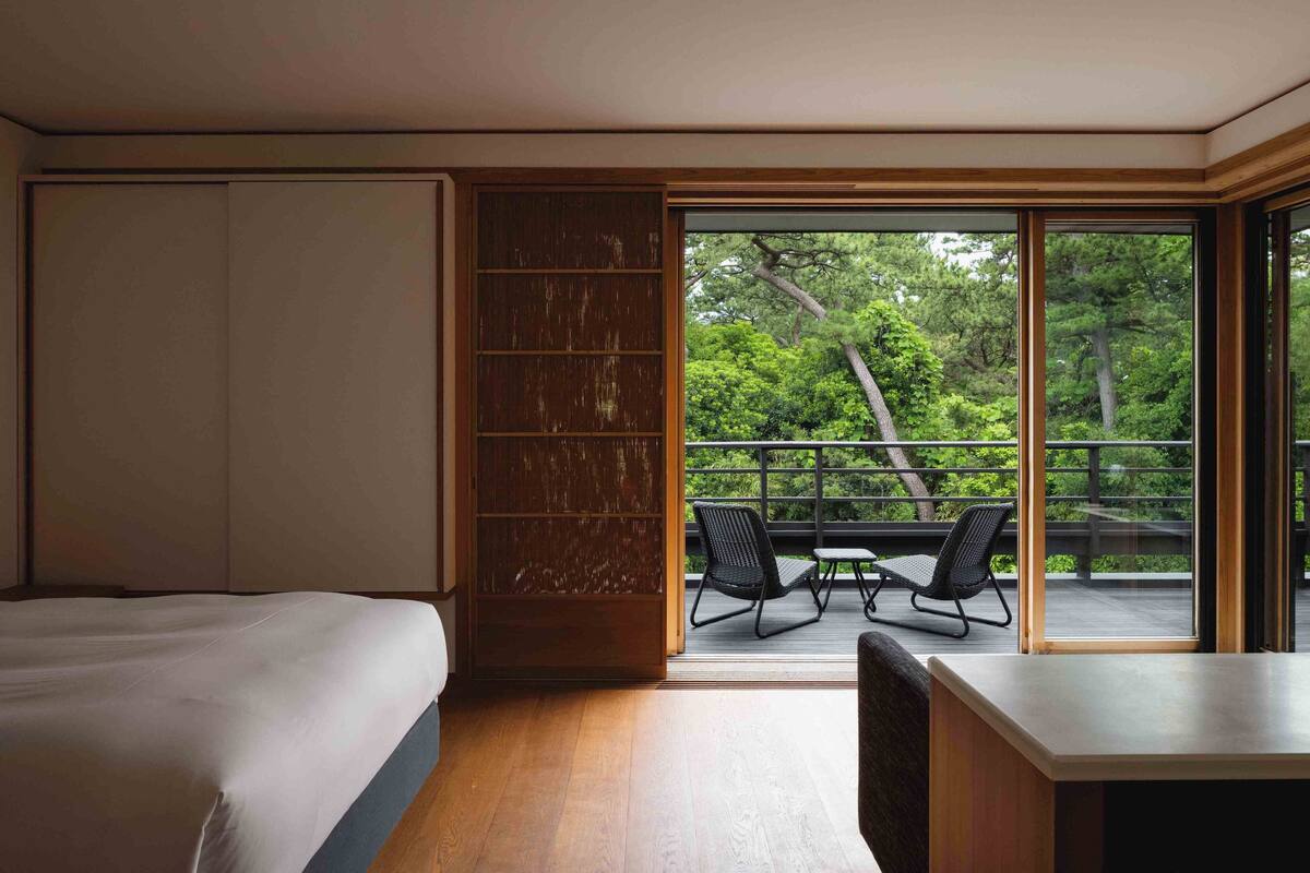 Ein Schlafzimmer mit einem großen Bett, einem Holzschrank und einer Glastür, die zu einem Außenbereich mit Tisch und Stühlen führt.