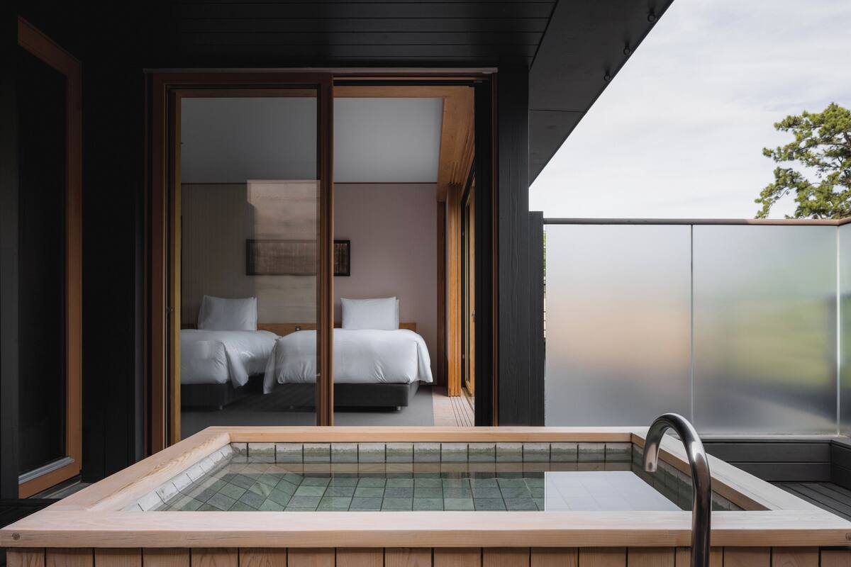 Ein modernes Hotelzimmer mit einer großen Schiebetür zu einem Schlafbereich, einem privaten Balkon und einer Whirlwanne.