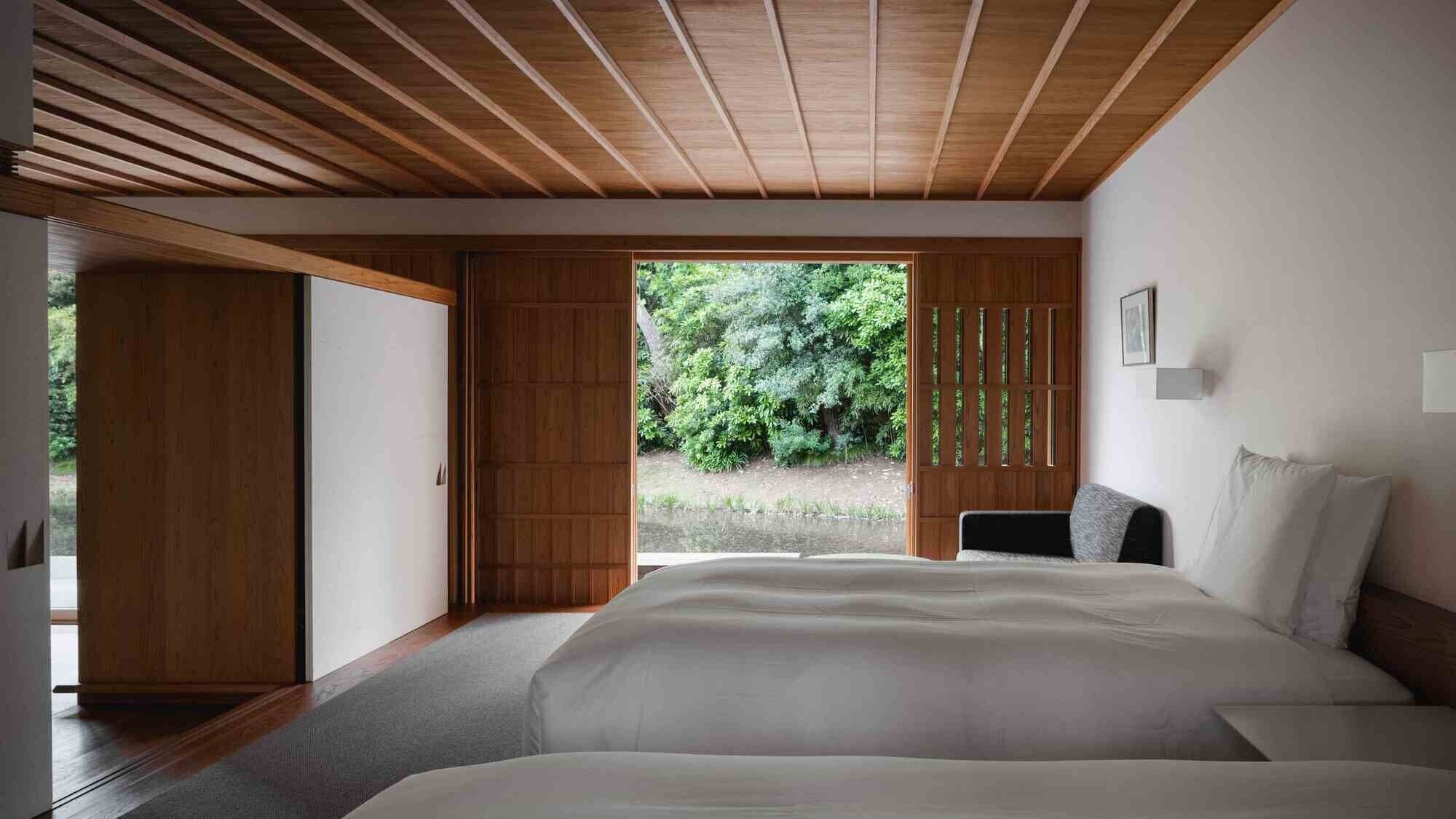 Un dormitorio con una cama grande, vigas de madera en el techo, una puerta corredera y vistas al verdor exterior.