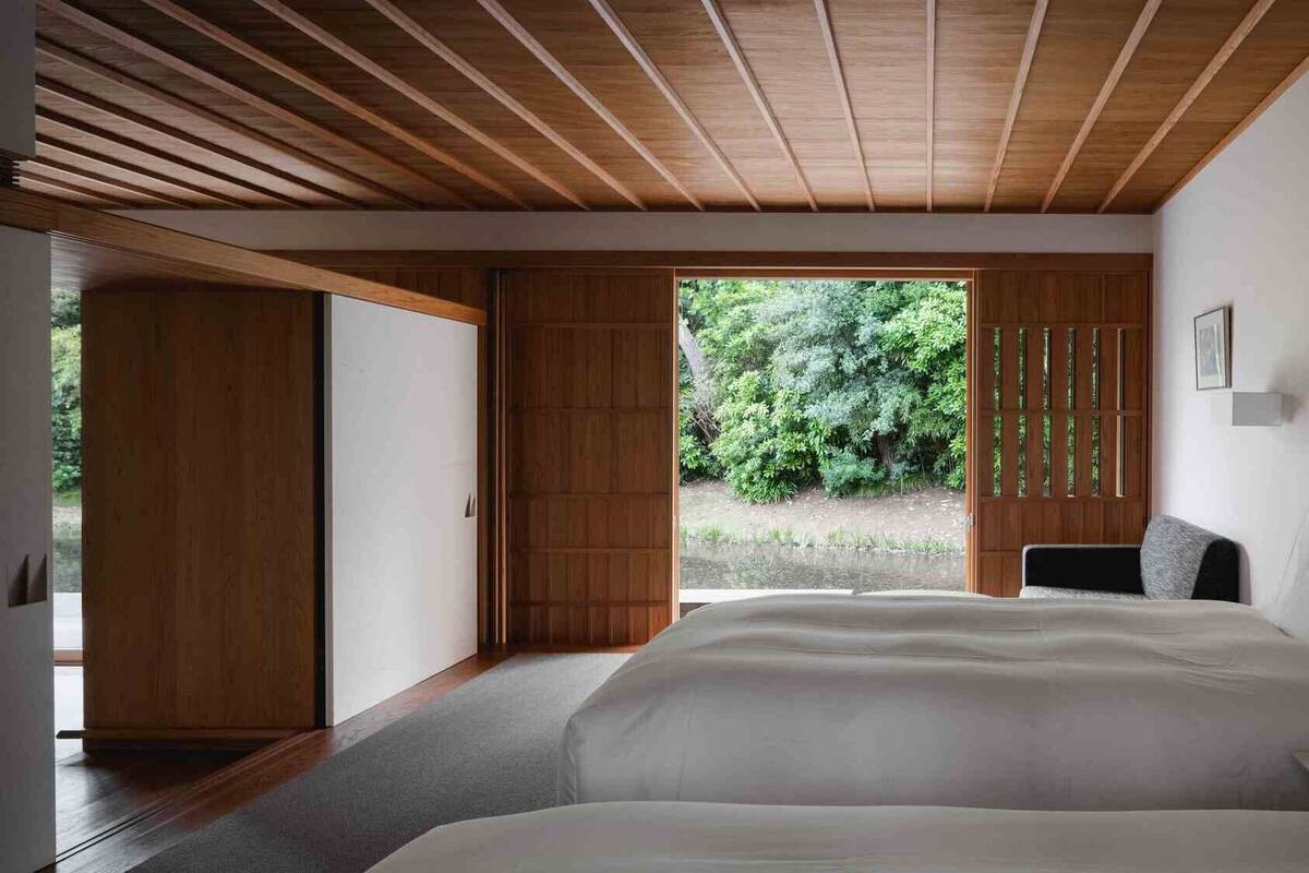 Ein Schlafzimmer mit einem großen Bett, Holzbalkendecke, einer Schiebetür und Blick auf Grünlandschaft.