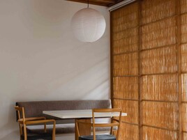 Quarto com parede de madeira, uma mesa branca, duas cadeiras de madeira e um lustre.