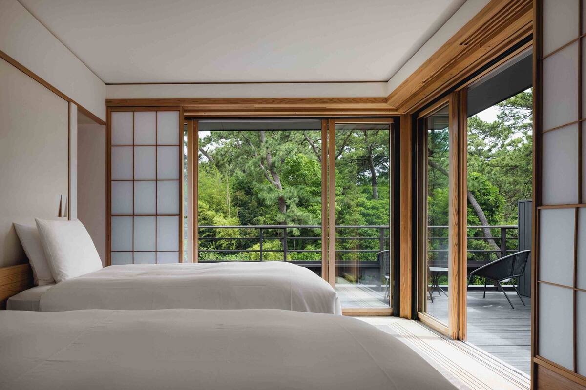 Ein Schlafzimmer mit einer großen Schiebeglasdoor zu einem Balkon mit Blick auf Bäume.