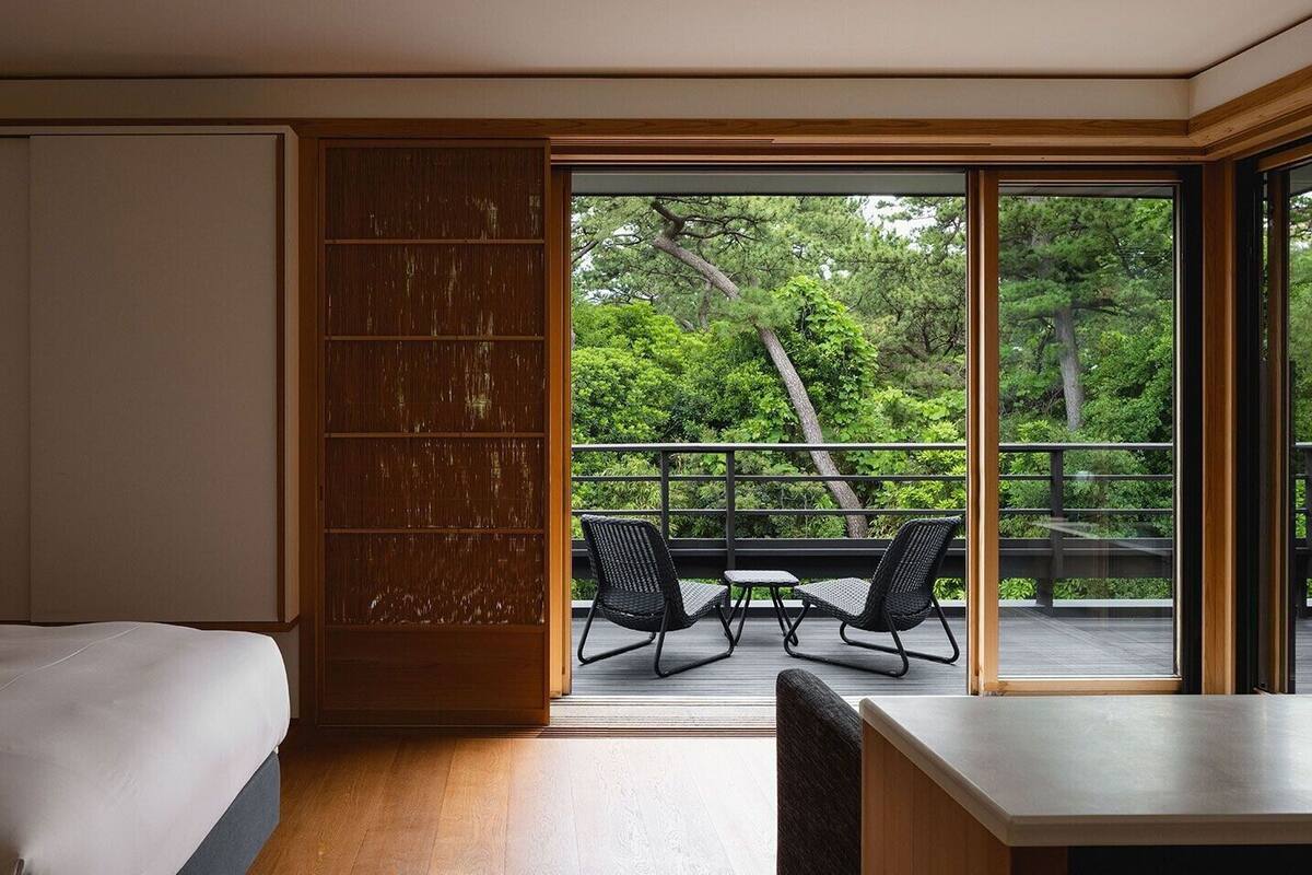 Ein Hotelzimmer mit einem Bett, einer Schiebetür zu einem Balkon und Blick auf Bäume.