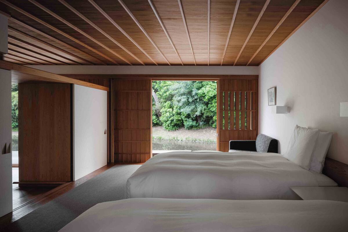 Ein Schlafzimmer mit einem großen Bett, Holzbalkendecke und Blick auf Grünfläche.