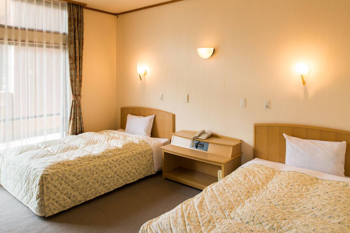 Ein Hotelzimmer mit zwei Betten, einem Nachttisch mit Telefon und Wandleuchten.
