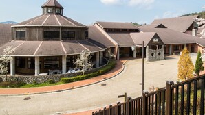 A hotel with a central courtyard, multiple buildings with pitched roofs, and a stone wall surrounding the area. - Gokurakuji Onsen Arcadia Village (Hatsukaichi)