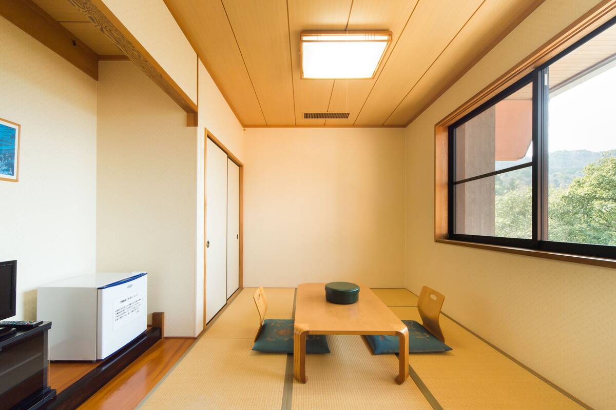 Ein Zimmer mit Tatami-Matten, einem niedrigen Tisch, einem Fernseher und einem Schrank.