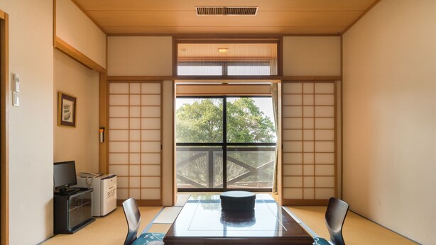 A traditional Japanese room with tatami flooring, a low table with a black object, and a view of a bridge outside the window. - Gokurakuji Onsen Arcadia Village (Hatsukaichi)