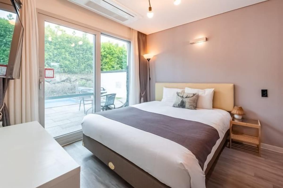 A modern hotel room with a large bed, a desk, and a sliding glass door leading to an outdoor area.