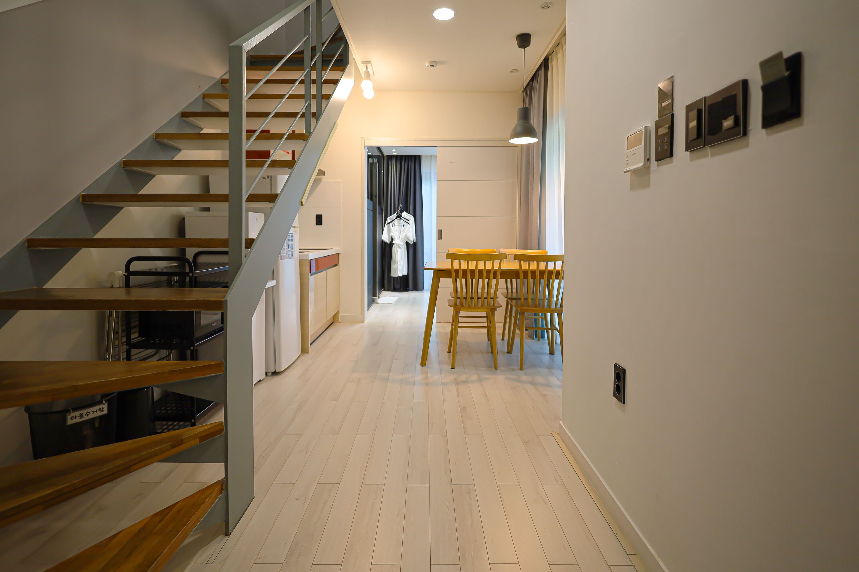A modern interior with a staircase, wooden flooring, a dining area with yellow chairs, and a coat hanging on the wall.