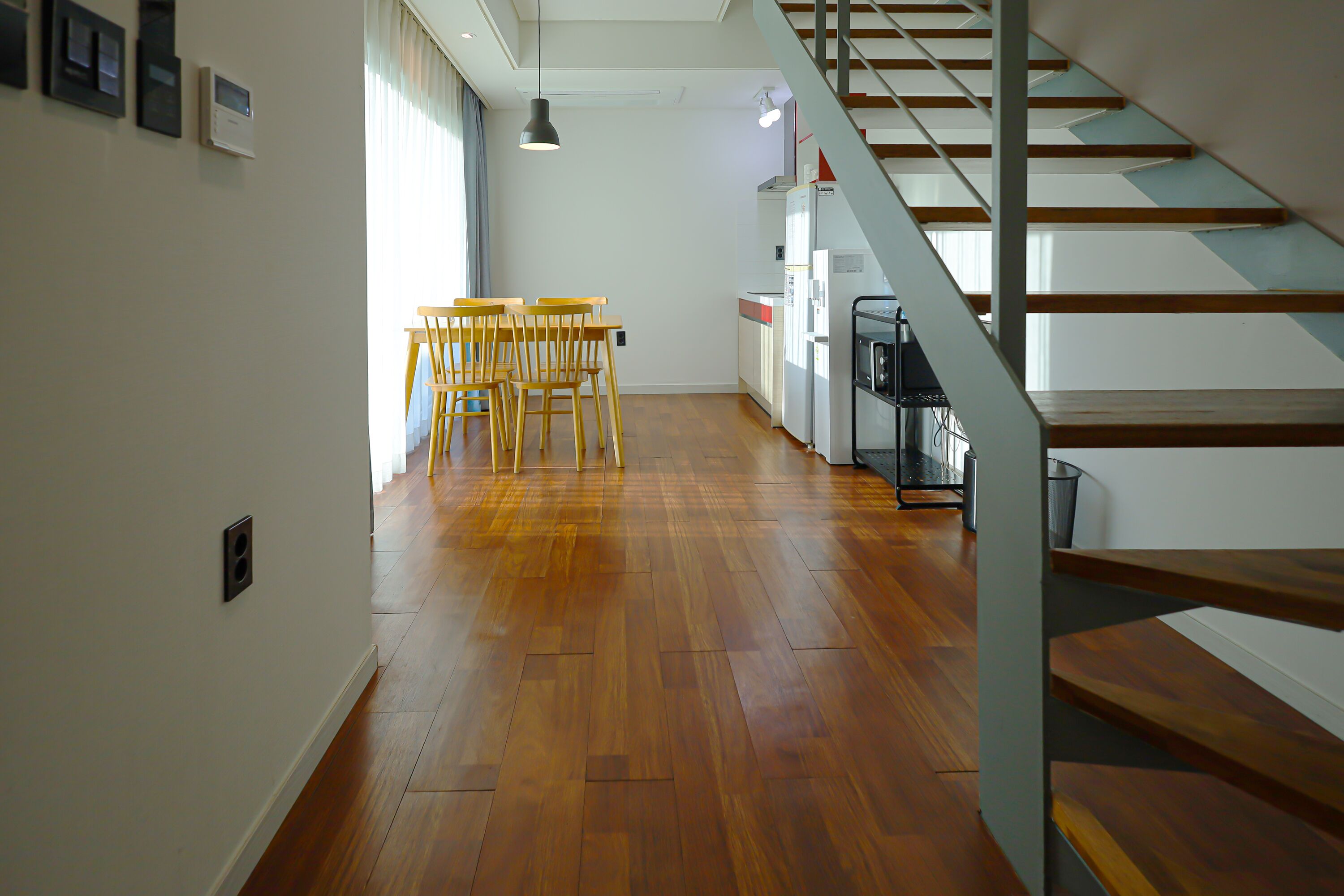 A modern kitchen with wooden flooring, a dining area with chairs, and a staircase.