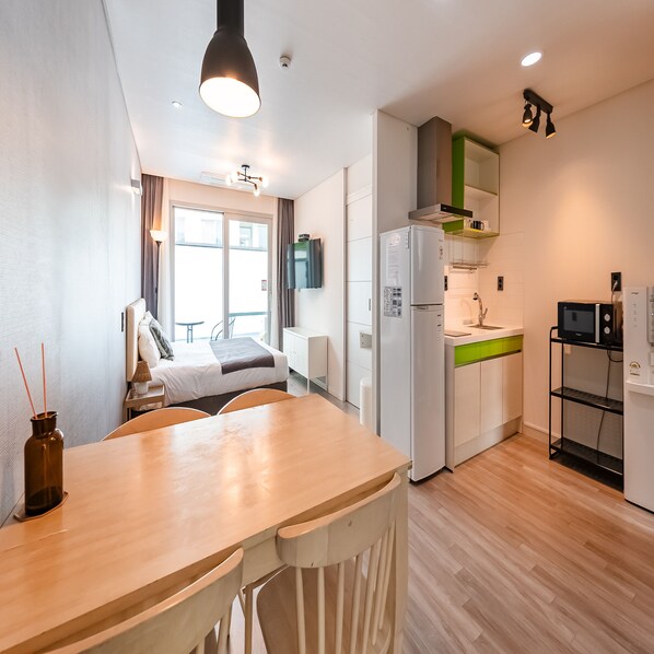 A compact hotel room with a kitchenette, a bed, a dining area, and a bathroom. - Pool & Villa Sorang (Jeju City)