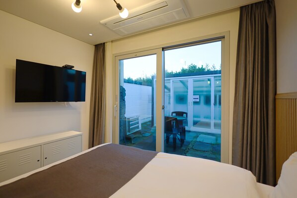 A hotel room with a bed, a TV mounted on the wall, a sliding glass door to the outside, and a small table and chair by the door. - Pool & Villa Sorang (Jeju City)