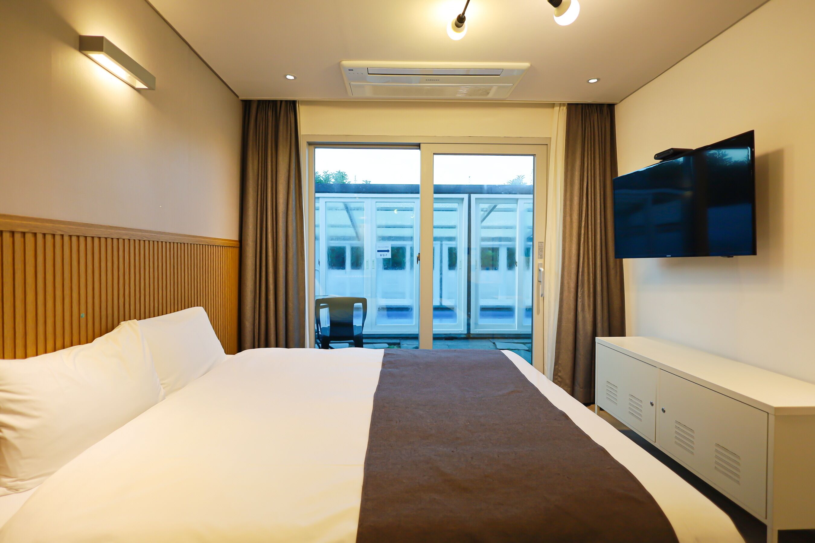 Habitación de hotel con cama, televisión, armario y vistas al exterior.