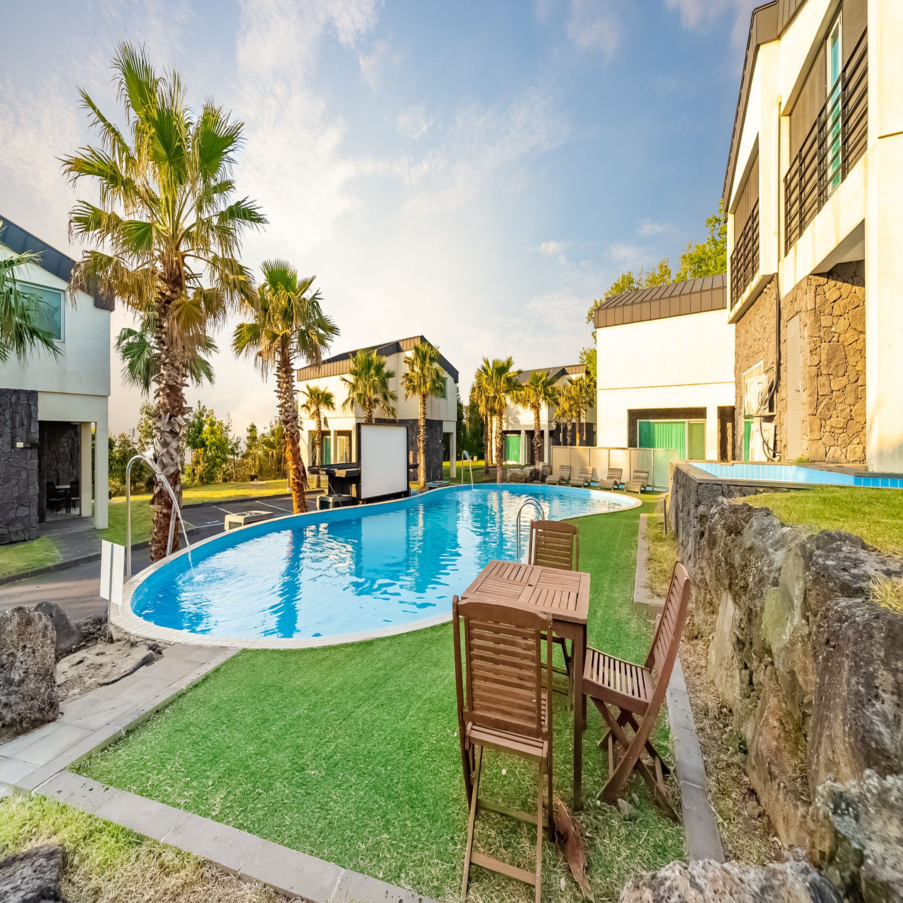 A swimming pool with a green lawn, palm trees, and a stone wall.
