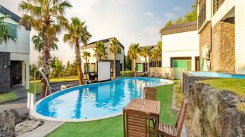 A swimming pool with a green lawn, palm trees, and a stone wall.