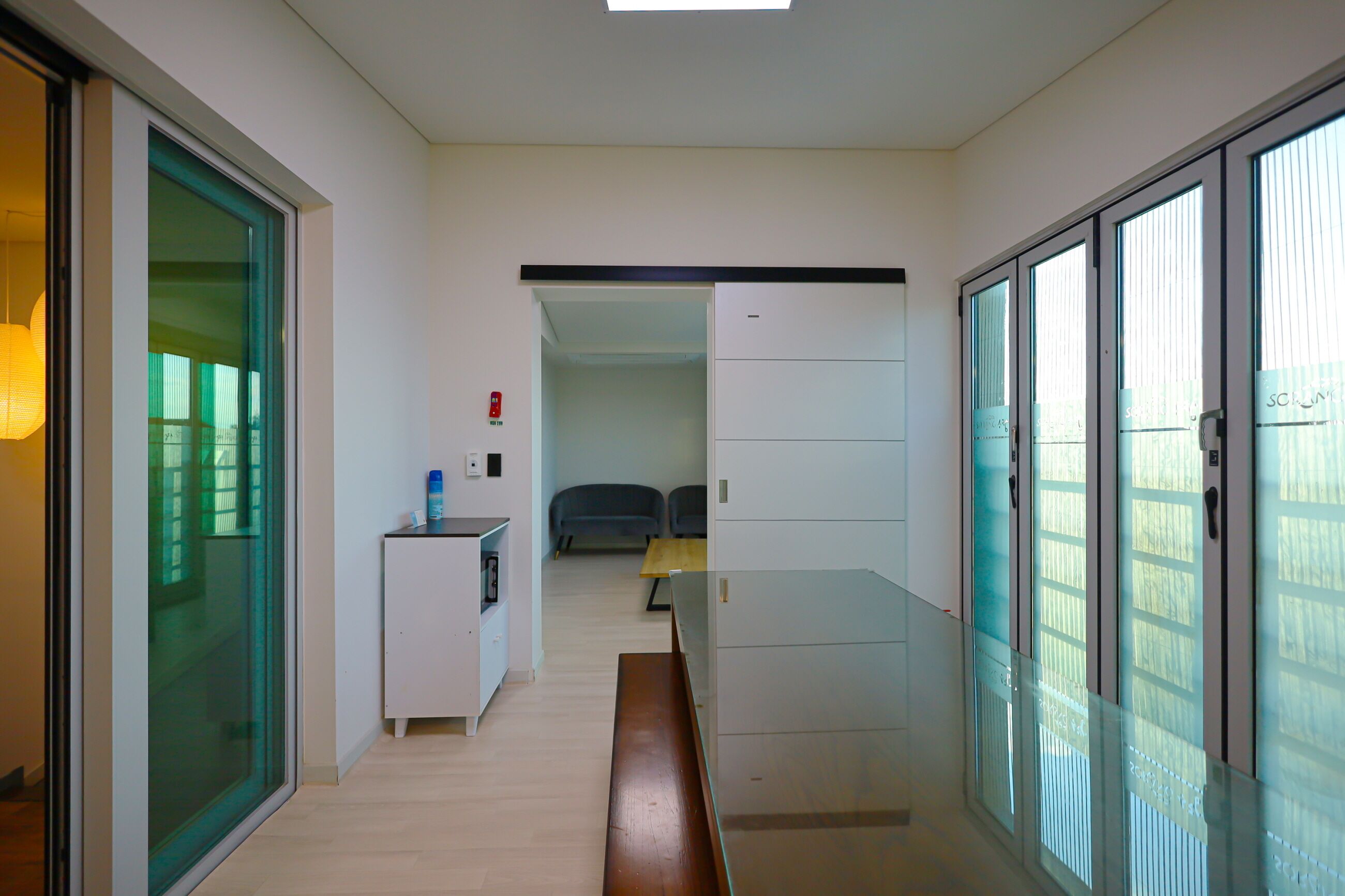 A corridor with a bench, a small table with a lamp, and a fire extinguisher on the wall.