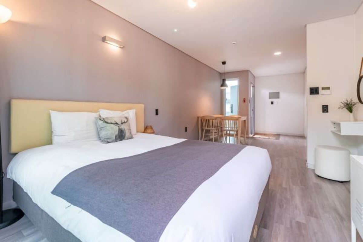 Une chambre d’hôtel moderne avec un grand lit, une table de chevet, une chaise et un petit bureau.
