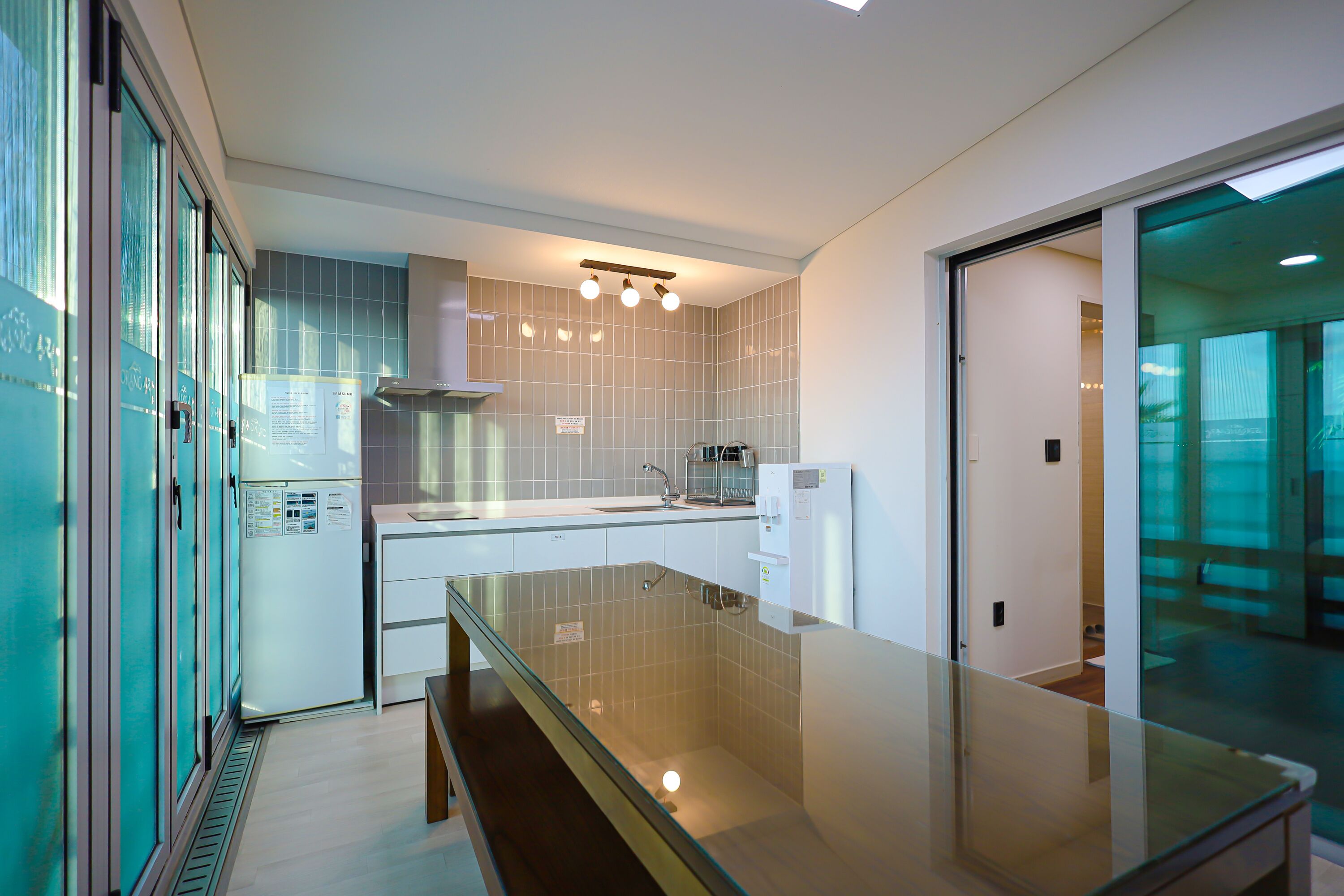 A modern kitchen with a glass-top island, white cabinets, and a stainless steel refrigerator.