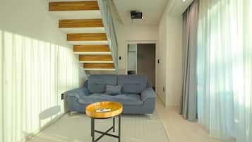 A modern living room with a grey sofa, a small wooden coffee table, and a staircase with wooden beams.