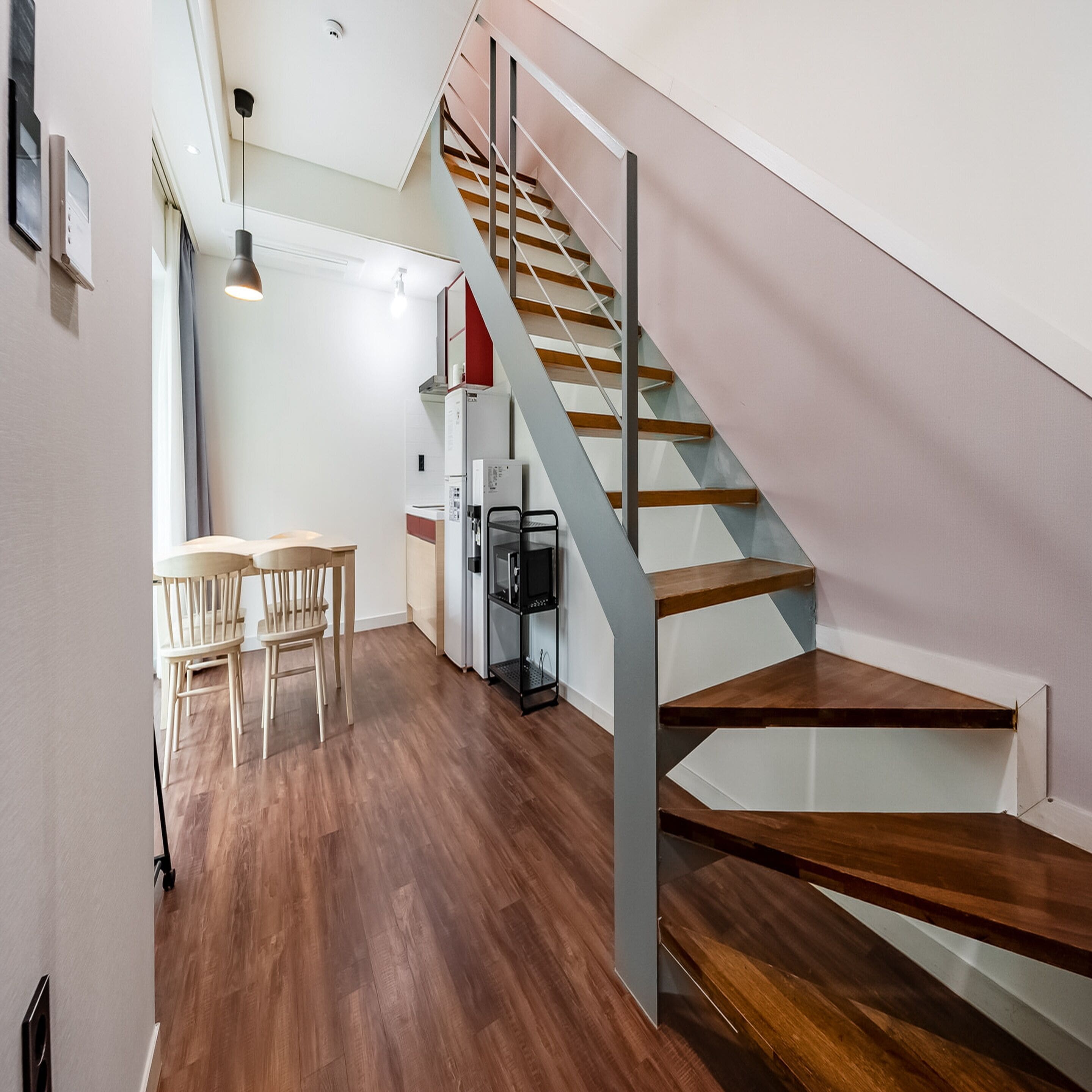 A modern kitchen with wooden flooring, a dining area with chairs, and a staircase with a metal railing.